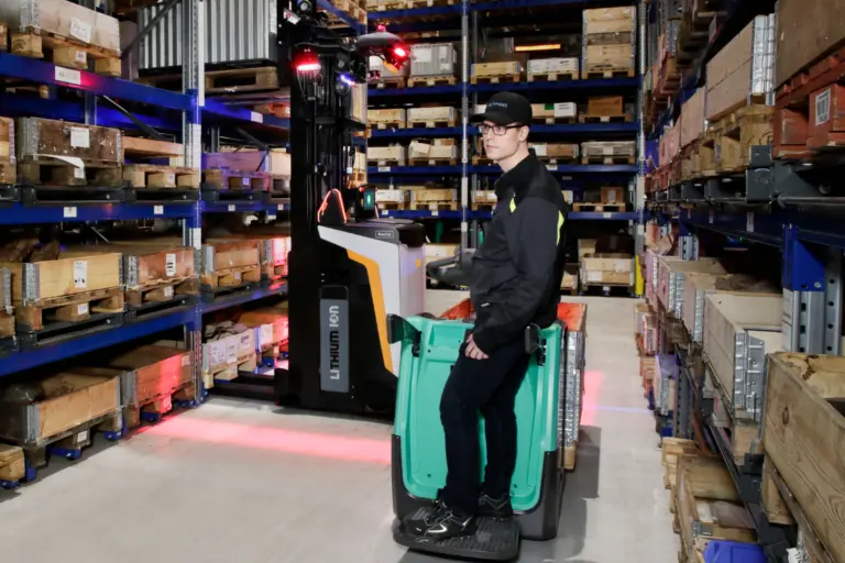 Chariot automatisé et chariot élévateur conduits par un opérateur évoluant dans un entrepôt avec éclairages de sécurité projetés au sol.