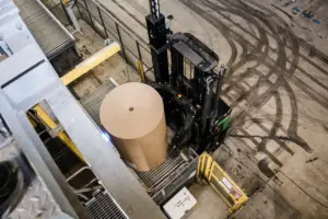 AGV Logisnext équipé d'une pince à bobines manipulant une bobine de papier ou de carton dans un environnement industriel.