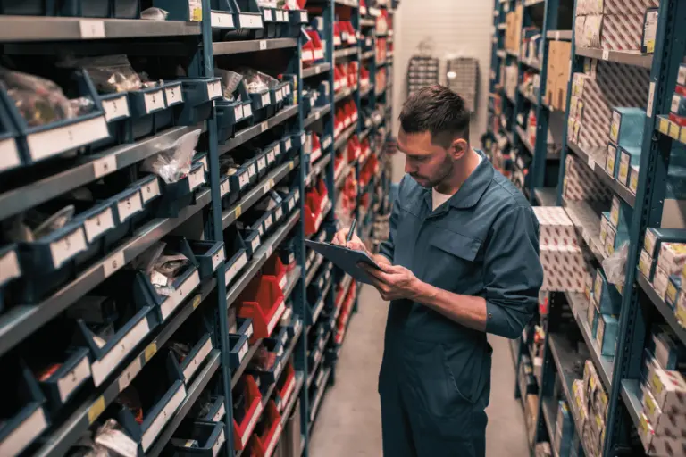 Personne consultant des pièces détachées dans un magasin de stockage équipé de rayonnages.