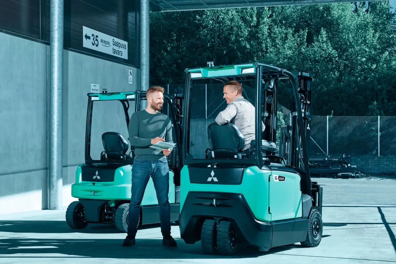 Chariot élévateur électrique Logisnext présenté devant un bâtiment professionnel avec plusieurs personnes à proximité.