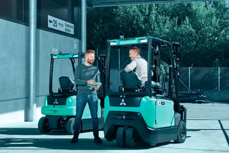 Chariot élévateur électrique Logisnext présenté devant un bâtiment professionnel avec plusieurs personnes à proximité.
