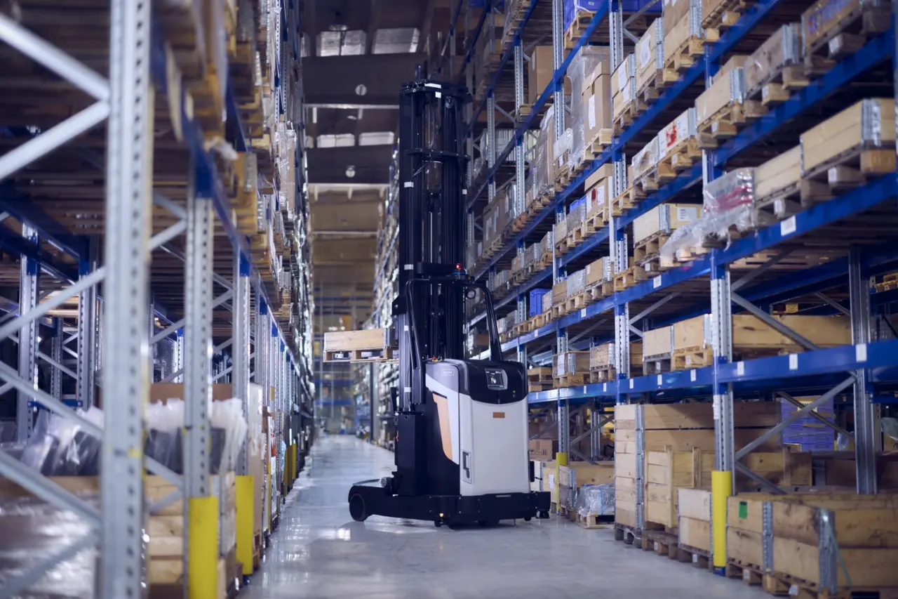 AGV Logisnext circulant dans une allée de stockage entre des rayonnages industriels et des palettes.