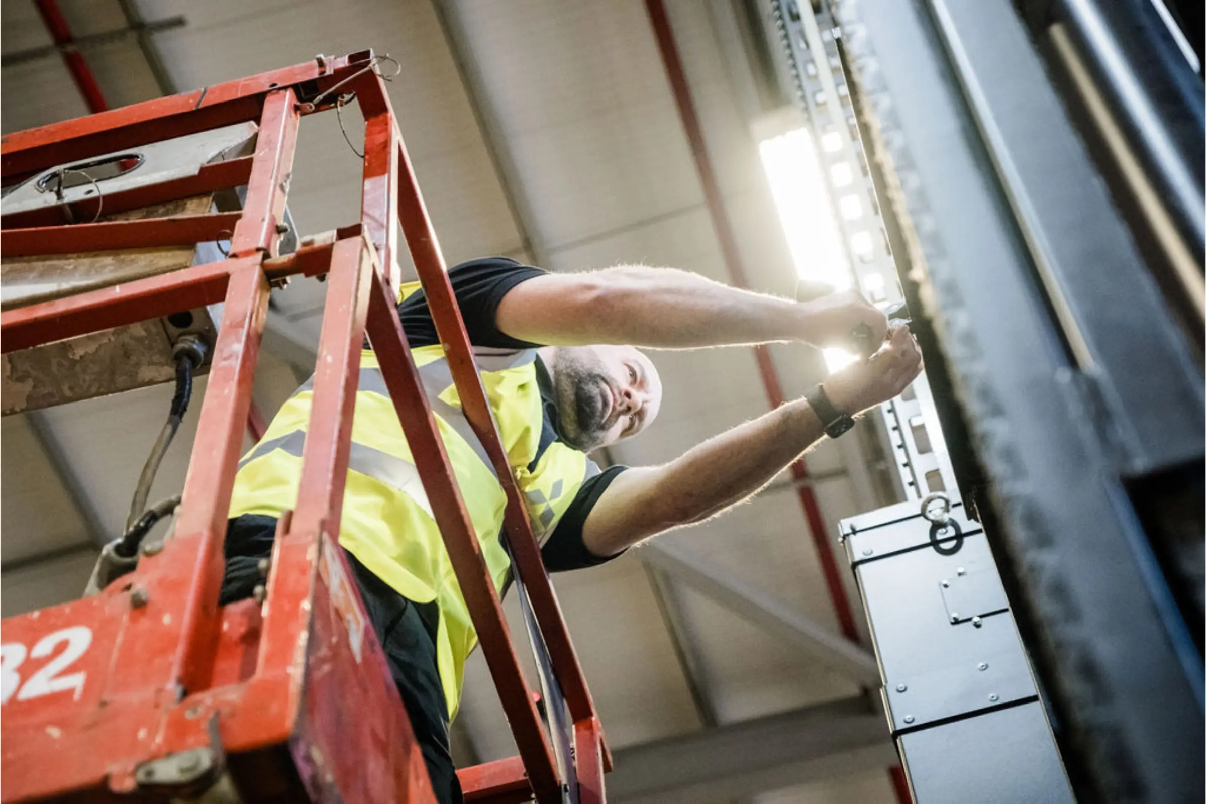 Technicien réalisant une intervention de maintenance sur un équipement de manutention depuis une nacelle.