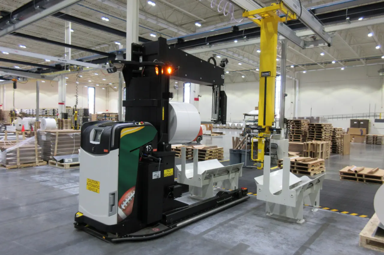 AGV Logisnext équipé d'une fourche porte-bobines manipulant une bobine dans une installation de l'industrie de l'emballage.