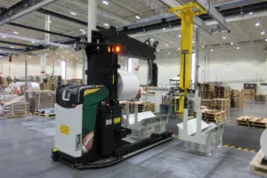 AGV Logisnext équipé d'une fourche porte-bobines manipulant une bobine dans une installation de l'industrie de l'emballage.