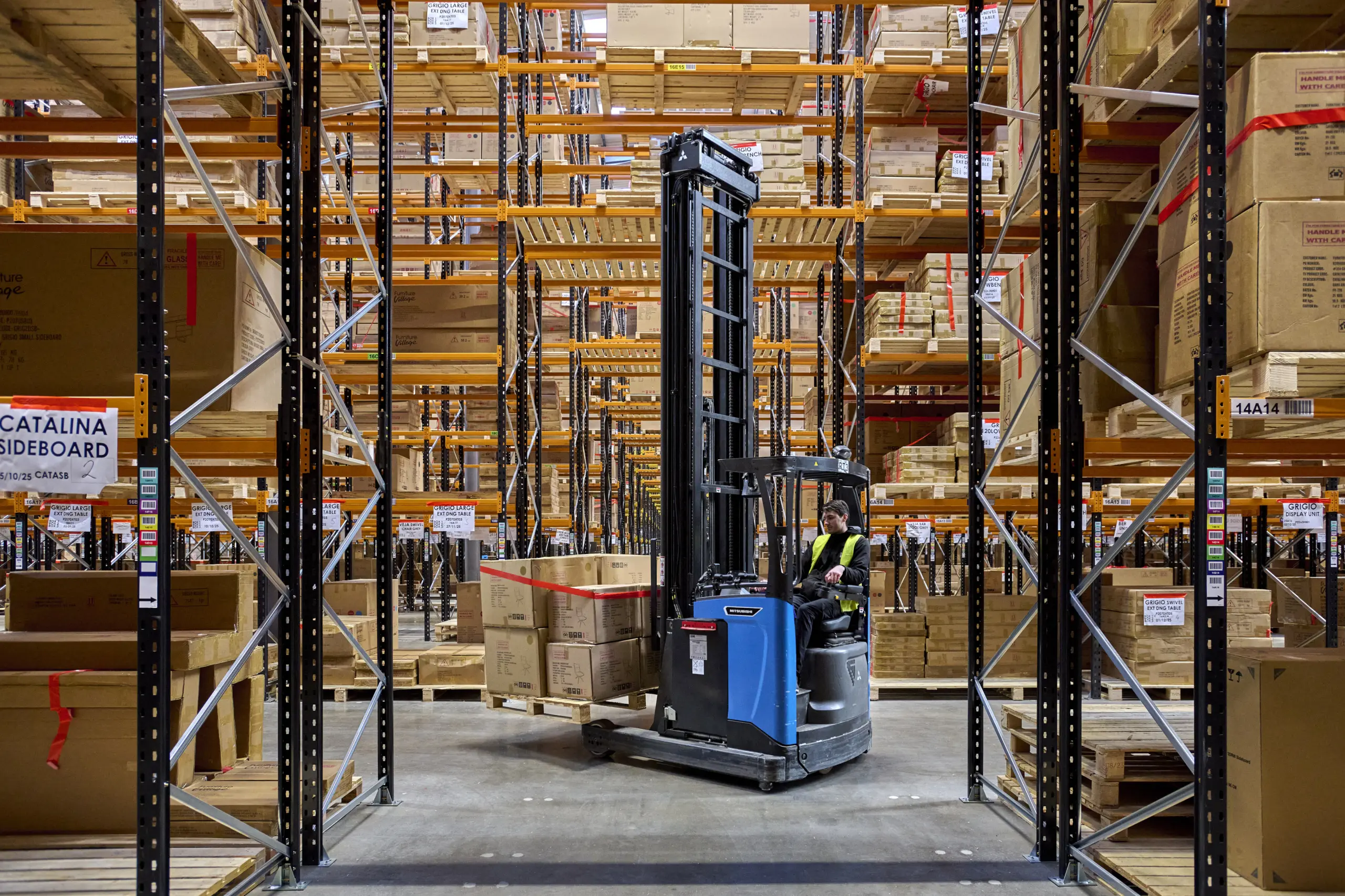 Chariot rétractable évoluant dans une allée de stockage entre des rayonnages à palettes.