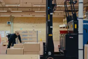 AGV à mât rétractable Logisnext opérant dans une zone logistique où des colis sont préparés manuellement.